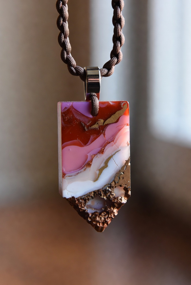 Fordite shield-cut pendant — pink, copper, and cream tones on twisted cord